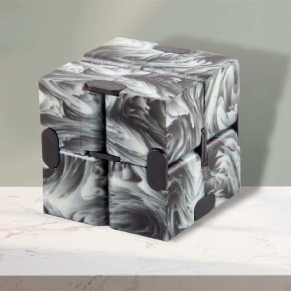 Cubo Infinito preto com padrão marmoreado em tons de cinza e branco, com cantos arredondados e detalhes em preto, colocado sobre uma superfície de mármore.