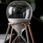 Ampulheta de laboratório com esfera de vidro transparente, areia branca no interior, suportada por uma estrutura de metal dourado.