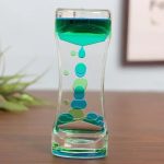 Ampulheta de óleo líquido com cores verdes e azuis, mostrando o fluxo de óleo de cima para baixo em um recipiente de vidro.