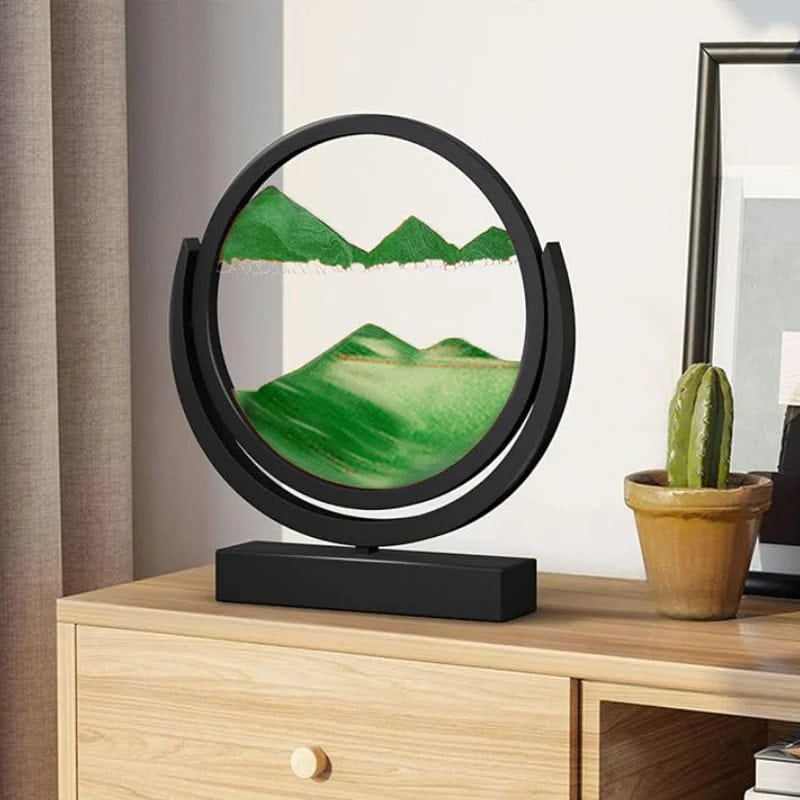 Lâmpada decorativa com painel de paisagem montanhosa verde, estrutura circular preta, colocada numa mesa de madeira com uma planta de cacto ao lado.