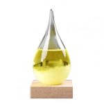 Gota de vidro com cristais coloridos, preenchida com líquido amarelo, colocada sobre base de madeira, usada para demonstração de física e ciência.