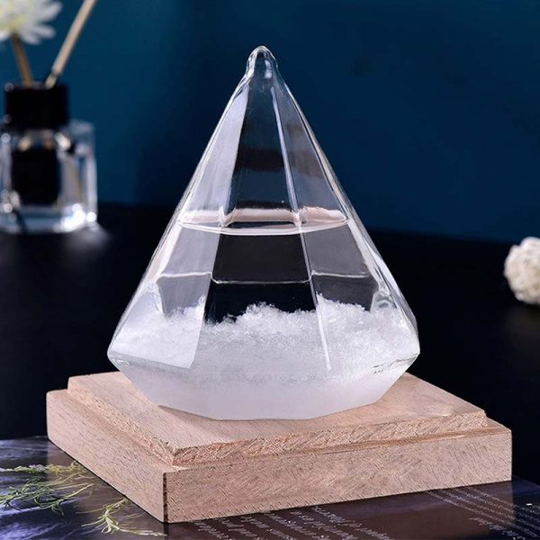 Cristais transparentes em forma de pirâmide com base de madeira, usado como barómetro de ciência, com fundo escuro e objetos de decoração ao fundo.