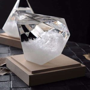 Cristal transparente com líquido, montado numa base de madeira, usado para demonstrações científicas de pressão atmosférica.