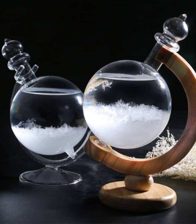 Reagente de cristal com suporte de madeira, contendo líquido transparente e cristais brancos no fundo, com fundo escuro.