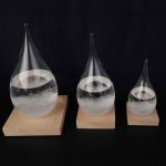 Três cristais em forma de gotas de água, de tamanhos diferentes, colocados sobre bases de madeira, com líquido transparente dentro.