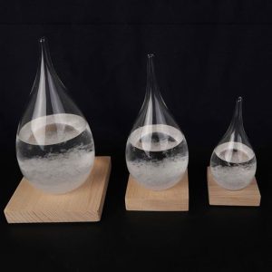 Três cristais em forma de gotas de água, de tamanhos diferentes, colocados sobre bases de madeira, com líquido transparente dentro.