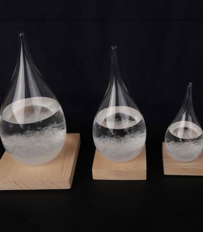 Três cristais em forma de gotas de água, de tamanhos diferentes, colocados sobre bases de madeira, com líquido transparente dentro.