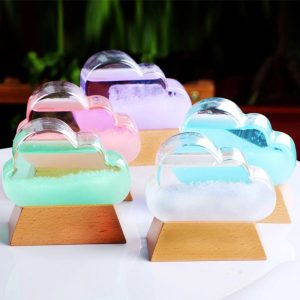 Conjunto de cinco nuvens de cristal de cores diferentes, cada uma colocada sobre uma base de madeira, com fundo de plantas verdes.
