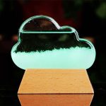 Cristal em forma de nuvem com líquido verde fluorescente, apoiado numa base de madeira, usado para demonstrações científicas.