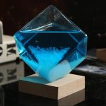 Cristais de sal azuis em forma de cubo, equilibrados sobre uma base de madeira, com fundo escuro e iluminação que realça a transparência e a cor.