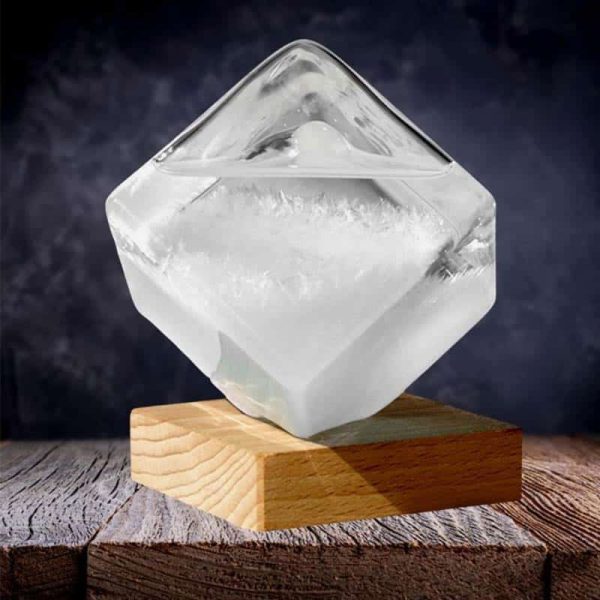 Cristal de sal de Rocha transparente com forma de cubo, colocado sobre uma base de madeira, com fundo escuro e iluminação que realça a sua transparência e detalhes.