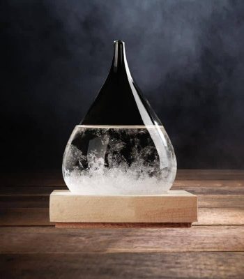 Cristal de forma gota com efeito de tempestade, parcialmente cheio de líquido, colocado numa base de madeira escura.