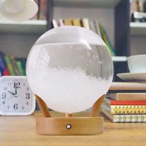 Bola de cristal decorativa com base de madeira, mostrando efeito de nevoeiro no interior, em ambiente de escritório com livros ao fundo.