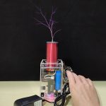 Bobina de Tesla de Arma com faíscas visíveis, tubo vermelho e estrutura transparente, controlada por uma mão que ajusta o dispositivo.