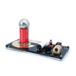 Bobina de Tesla mini com esfera metálica brilhante, componentes eletrónicos visíveis, e base preta com detalhes dourados, demonstrando uma experiência de eletricidade estática.