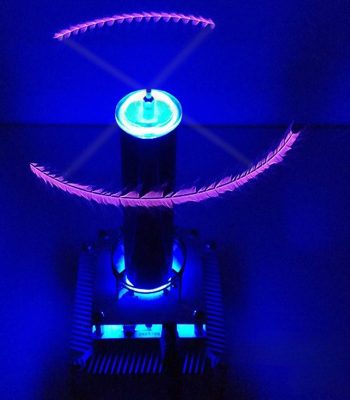 Bobina de Tesla miniatura a emitir faíscas azuis com efeitos de luzes violetas e roxas, destacando-se num ambiente escuro com faíscas visíveis.