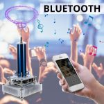 Bobina de Tesla em miniatura a emitir faíscas azuis, conectada via Bluetooth a um smartphone a transmitir música, com pessoas ao fundo a dançar.