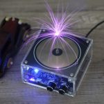 Bobina de Tesla musical a gerar faíscas violetas com efeito de plasma visível, circuito eletrônico e controle de volume na base de acrílico transparente.