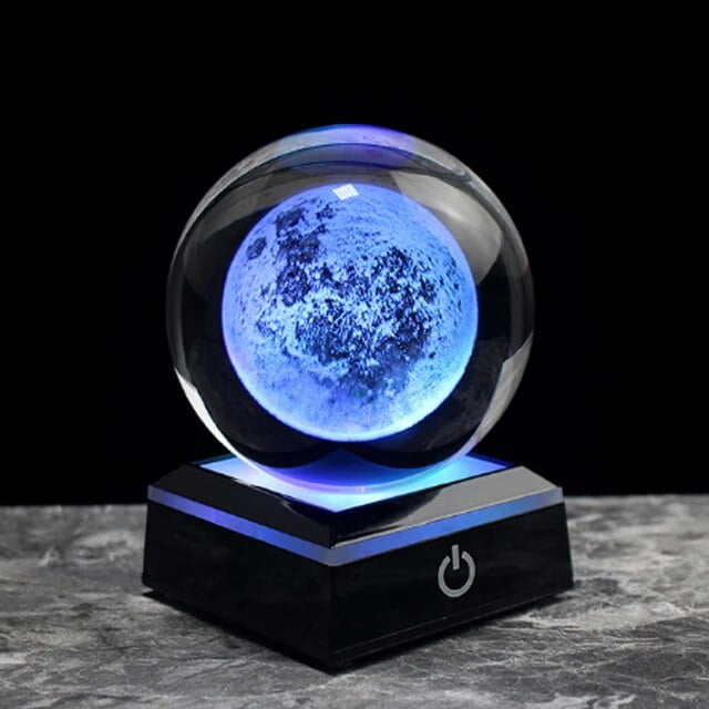 Lâmpada de cristal com efeito lunar azul, base preta com botão de ligar, iluminação suave e detalhes da superfície lunar visíveis.