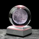Bola de cristal com efeito lunar, iluminada por luz rosa, sobre base metálica com botão de energia, fundo preto.