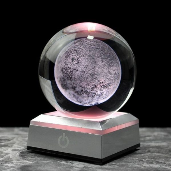 Bola de cristal com efeito lunar, iluminada por luz rosa, sobre base metálica com botão de energia, fundo preto.