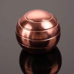 Bola giroscópio de metal rosé com linhas curvas e acabamento brilhante, refletindo a luz sobre uma superfície escura.