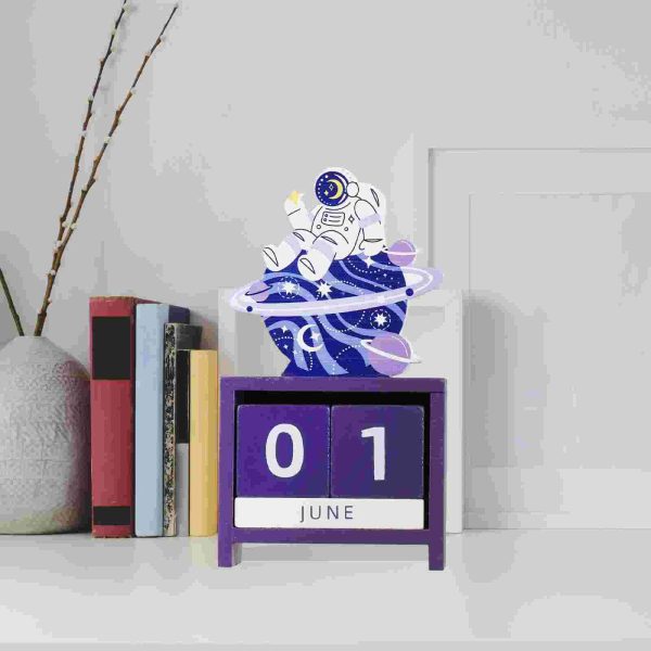 Calendário perpétuo com astronauta em estilo cartoon, decorativo, em tons de violeta e branco, com planetas e estrelas ao redor, em uma mesa branca ao lado de livros e uma planta.