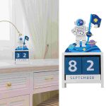 Calendário perpétuo com tema de astronauta, com figuras espaciais, planeta e bandeira, em cores violeta e azul, em uma mesa de madeira.