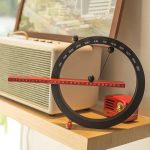 Relógio de calendário perpétuo magnético com ponteiro móvel, mostrando os meses e dias do ano, colocado numa superfície de madeira ao lado de um rádio antigo.