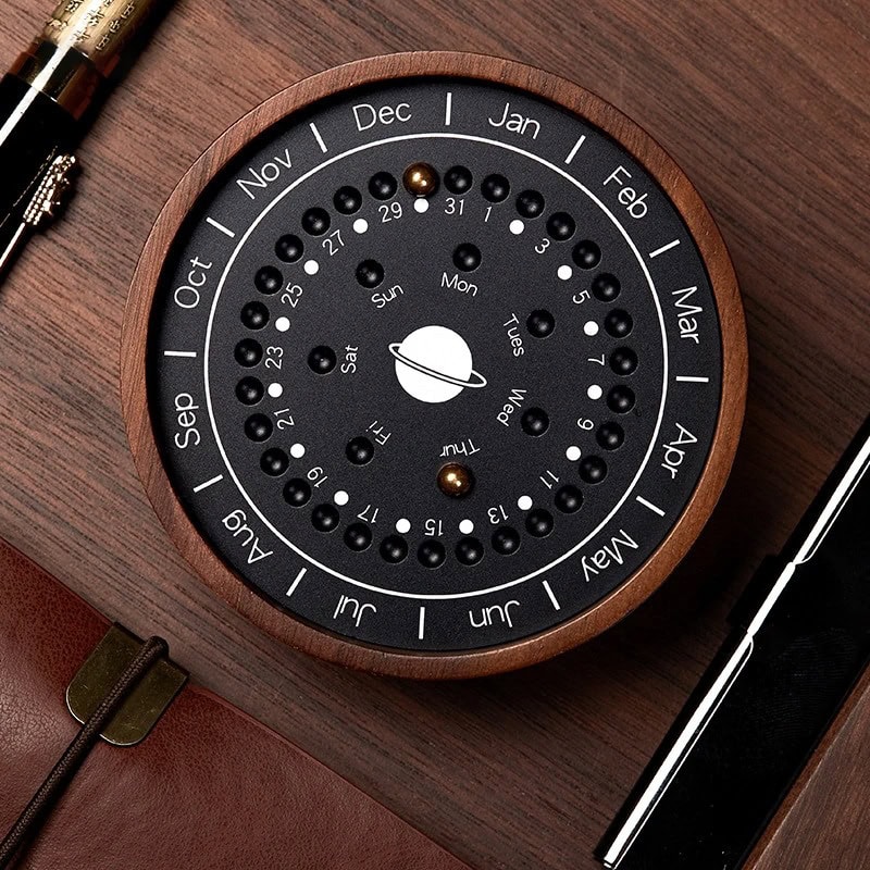 Relógio de calendário perpétuo com design circular, mostrando meses, dias e fases da lua, com detalhes em preto e branco e uma moldura de madeira.