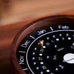 Calendário perpétuo magnético com meses, dias e fases da lua em madeira escura, detalhes visíveis de perto.