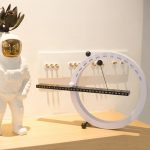 Relógio de calendário perpétuo magnético com ponteiro de dias, meses e anos, colocado numa superfície de madeira junto a uma figura de astronauta decorativa.