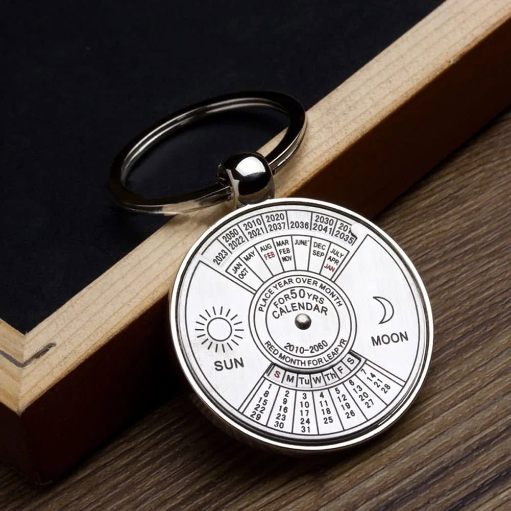 Chaveiro com calendário perpétuo Chaveiro metálico com calendário perpétuo, mostrando meses, dias e fases da lua, com detalhes em preto e branco.