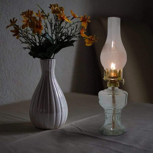 Vaso de cerâmica branco com flores amarelas e candeeiro a óleo vintage aceso em ambiente escuro.