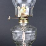 Candeeiro a óleo vintage com cúpula de vidro transparente, base de vidro decorativa e mecanismo de acendimento manual.