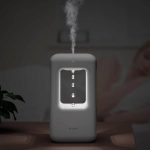 Lâmpada de plasma com gotas de água suspensas, iluminação LED ao redor, em ambiente escuro, com uma pessoa ao fundo.
