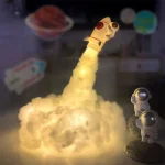 Candeeiro de mesa com forma de astronauta a lançar um foguete, com luzes e detalhes em cores metálicas e vermelhas, decorando um ambiente de ciência infantil.