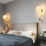 Candeeiros de parede com forma de lua, com detalhes de astronauta, iluminam uma parede de quarto com luz quente, criando ambiente acolhedor.