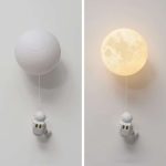 Candeeiro de parede com forma de lua, iluminação quente, com astronauta pendurado por fio, decorativo para quarto infantil ou científico.