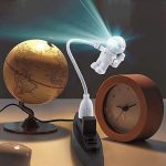 Luminária de astronauta com luz LED, conectada a uma base de tomada, ao lado de um globo terrestre dourado e um relógio de madeira.
