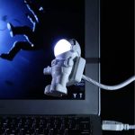 Miniatura de astronauta em LED com capacete brilhante, conectado a um computador portátil, ideal para decoração de ciência e gadgets.