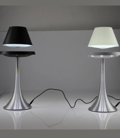 Dois candeeiros com abajures em levitação, um com abajur preto e outro com abajur branco, ligados por cabos elétricos, sobre uma superfície branca.