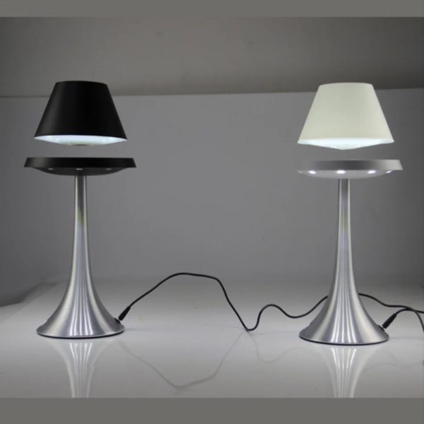 Dois candeeiros com abajures em levitação, um com abajur preto e outro com abajur branco, ligados por cabos elétricos, sobre uma superfície branca.