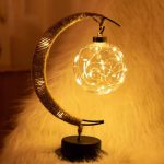 Luminária decorativa com forma de lua crescente, contendo uma esfera de vidro com luzes LED internas que imitam estrelas.