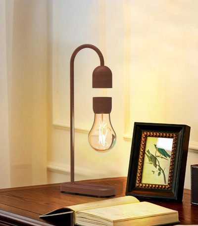 Candeeiro de mesa com lâmpada de filamento exposta, estrutura de madeira e design moderno, colocado numa mesa de madeira com quadro decorativo ao lado.