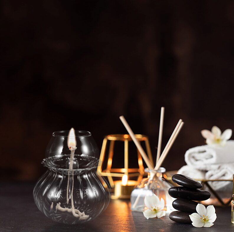 Velas acesas em frascos de vidro, pedras empilhadas, flores brancas e toalhas de algodão em ambiente de spa relaxante.