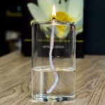 Vela acesa dentro de um vidro transparente com água, com uma flor branca ao fundo.