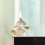 Candeeiro de mesa a óleo quadrado com chama acesa, vidro transparente e base de suporte, colocado numa superfície plana.