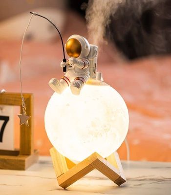 Miniatura de astronauta sentado na lua, segurando uma vara de pesca, com luz quente e base de madeira.