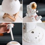 Luminária de mesa em forma de planeta com suporte de madeira, luminária de astronauta com detalhes em vermelho e branco, e uma base de tecido branco com orifícios.
